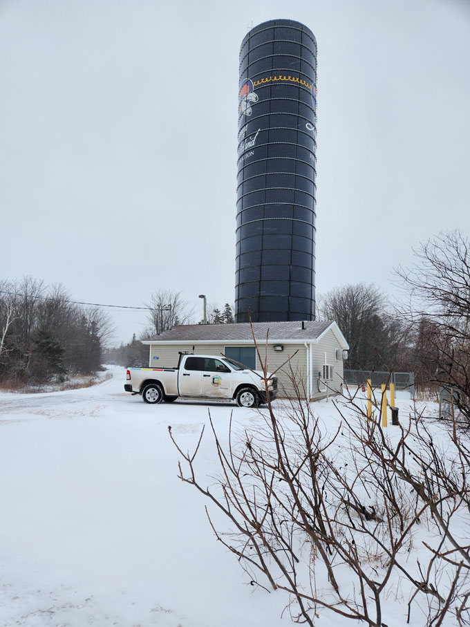 Une camionette blanche arbore le logo du AFNWA. Le véhicule est stationné devant une cabane. Derrière la cabane, on y voit un silo avec le logo de la Première Nation.
