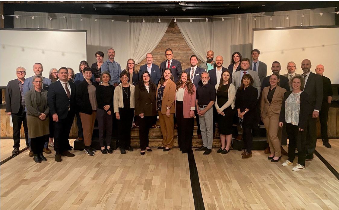  Un groupe de 33 personnes qui ont participé au Comité consultatif sur l&rsquo;accès à la justice dans les deux langues officielles se tenant ensemble dans une salle de conférence lors de leur réunion annuelle à Canmore, en Alberta.